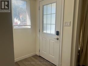 Oshawa (Eastdale) apartment for rent - A white door with a glass panel is in a room with a window and a light switch on the wall.