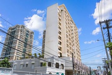 San Juan apartment for rent - A white building with a green stripe on the bottom is in the foreground with a blue sky and clouds in the background.