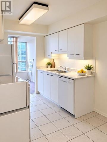 Mississauga (City Centre) condo for rent - A white kitchen with a refrigerator on the left and a sink with a bowl of fruit on the counter.