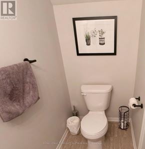 Oakville (Ro River Oaks) condo for rent - A white toilet in a small bathroom with a framed picture of plants and a towel rack.