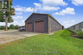 Blandford-Blenheim apartment for rent - A large, dark-colored metal building with a garage door is situated in a grassy area with a car parked in front.