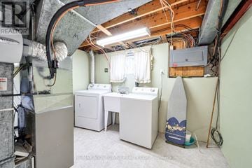 Burlington (Shoreacres) apartment for rent - A small, unfinished basement with a washer and dryer, a desk, and a surfboard.