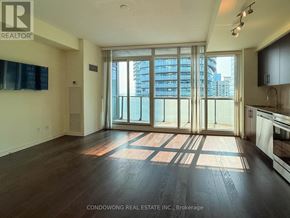 Toronto (Waterfront Communities) condo for rent - A large, empty room with wooden floors and a view of a city skyline through floor-to-ceiling windows.