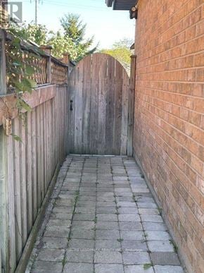 Barrie (Northwest) apartment for rent - A narrow alleyway with a wooden fence on one side and a brick wall on the other.