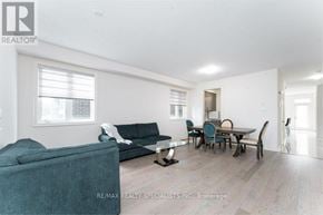 Hamilton (Waterdown) apartment for rent - A living room with a grey couch, a black sofa, a wooden dining table with chairs, and a white wall with a window.