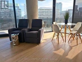 Toronto (Moss Park) condo for rent - A modern living room with a grey sofa, a white table and chairs, and a large window with a view of the city.