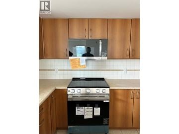 Port Moody apartment for rent - A black oven with a stove top sits in a kitchen with wooden cabinets.