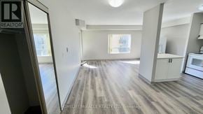 Waterloo multi-family for rent - A spacious room with wooden flooring and a kitchen area with white cabinets.