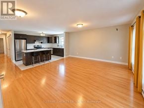 Ottawa fourplex for rent - A well-lit, empty living room with wooden flooring and a kitchen area in the background.