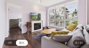 Surrey apartment for rent - A living room with a grey couch, a wooden table, a fireplace, and a large window showing a view of a building.