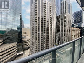 Toronto (Bay Street Corridor) condo for rent - A glass building with the letters "R" on it is in the foreground of a cityscape.