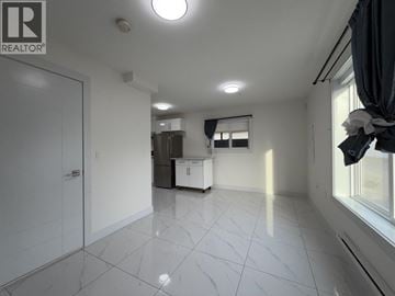 Vancouver apartment for rent - A spacious, empty room with white tiled flooring and a large window with curtains.