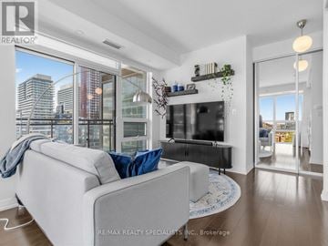 Toronto (Moss Park) condo for rent - A modern living room with a grey couch and a large window overlooking the city.