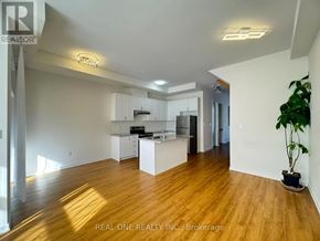 Markham (Wismer) townhouse for rent - A spacious room with wooden floors and white walls, featuring a kitchen area with white cabinets and appliances.