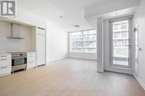 Toronto (Waterfront Communities) condo for rent - A spacious, empty room with a kitchen area to the left and a large window with a view of a building outside.