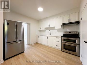 Toronto (Dovercourt-Wallace Emerson-Junction) apartment for rent - A kitchen with a stainless steel refrigerator and oven, white cabinets, and wooden flooring.