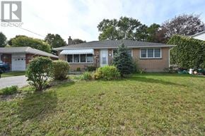 Oshawa (Centennial) apartment for rent - A house with a brown brick exterior and a white door is surrounded by a grassy area and some shrubbery.