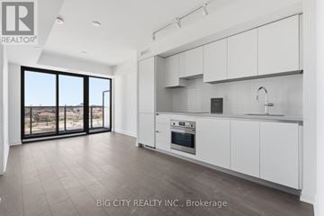 Toronto (Thorncliffe Park) condo for rent - A spacious kitchen with white cabinets and a large window overlooking a landscape.