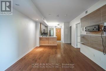 Ottawa condo for rent - A spacious room with wooden floors and white walls, featuring a kitchen area with a sink and cabinets.