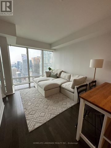Toronto (Waterfront Communities) condo for rent - A living room with a couch, a chair, a table, and a window with a view of the city.