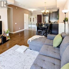 Toronto (Wexford-Maryvale) condo for rent - A living room with a grey couch and a kitchen in the background.