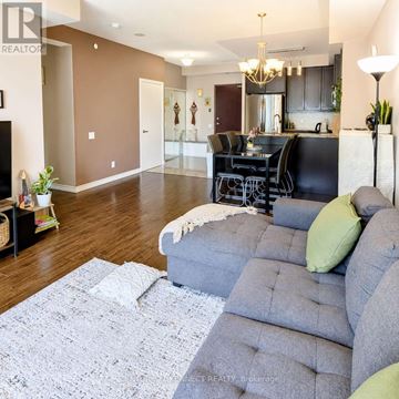 Toronto (Wexford-Maryvale) condo for rent - A living room with a grey couch and a kitchen in the background.
