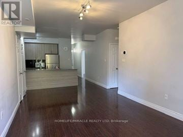 Brampton (Westgate) townhouse for rent - A spacious room with wooden flooring and white walls, with a kitchen area visible through the open door.