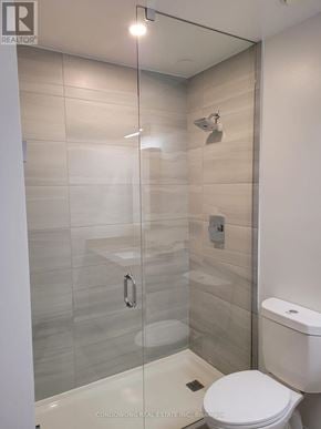 Markham (Commerce Valley) condo for rent - A white toilet in a modern bathroom with a glass shower stall.