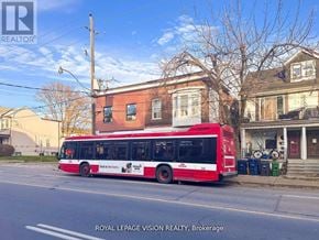 Toronto (Danforth Village-East York) multi-family for rent - A red bus is parked on the street in front of a house.