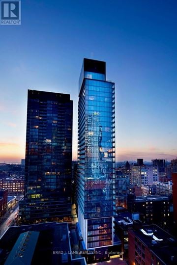 Toronto (Waterfront Communities) condo for rent - Two tall buildings with glass windows are illuminated from within at dusk.