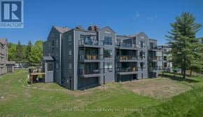 Huntsville (Chaffey) condo for rent - A large grey building with multiple balconies and a green lawn in front.