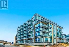 Oakville (Ga Glen Abbey) condo for rent - A modern multi-story building with a glass facade and a sign that reads "REALTOR".