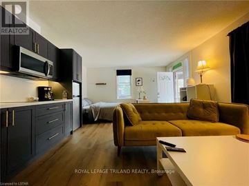 Central Elgin (Port Stanley) apartment for rent - A living room with a yellow couch and a kitchen area with black cabinets.