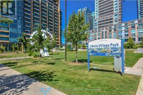 Toronto (Niagara) condo for rent - A sign for Liberty Village Park stands in a grassy area with trees and modern buildings in the background.