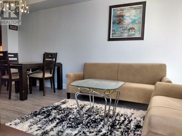 Markham (Unionville) condo for rent - A living room with a beige couch, a glass coffee table, and a framed painting on the wall.