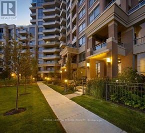 Markham (Unionville) condo for rent - A well-lit walkway leads to a building with balconies and a small tree in the foreground.