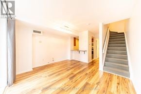 Toronto (Niagara) townhouse for rent - A spacious room with wooden floors and a staircase leading to another room.