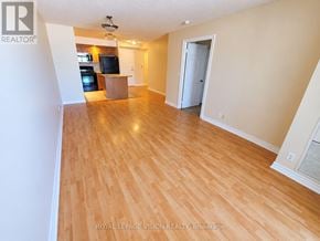 Markham (Unionville) condo for rent - A spacious room with wooden flooring and a kitchen area in the background.