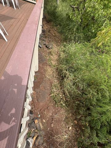 Kailua-Kona apartment for rent - A wooden deck with a red border is adjacent to a dirt path with greenery on the side.