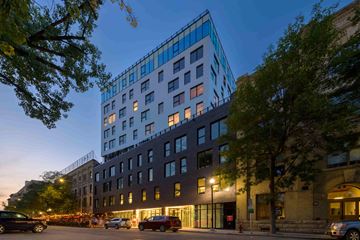 Winnipeg apartment for rent - A modern building with a glass facade is illuminated from within at dusk.