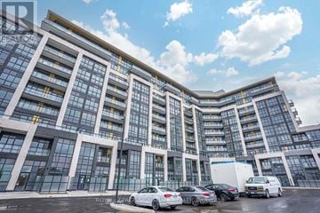 Oakville (Go Glenorchy) condo for rent - A modern building with a glass facade and a parking lot in front.