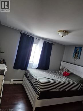 Kitchener condo for rent - A bedroom with a bed, nightstand, and window with blue curtains.