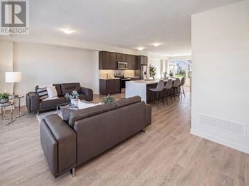 Cobourg townhouse for rent - A living room with a brown sofa and a dining table with chairs.