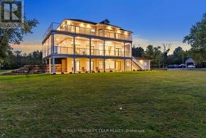 Fort Erie (Black Creek) apartment for rent - A large, modern house with a flat roof and glass walls is illuminated from within, showcasing its interior lighting.