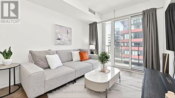 Toronto (Moss Park) condo for rent - A living room with a grey couch, a small table, and a painting on the wall.