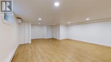 Toronto (Lawrence Park South) multi-family for rent - A spacious room with wooden flooring and white walls, with a realtor logo on the wall.