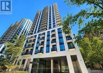 Toronto (Forest Hill South) condo for rent - A tall building with a balcony on the second floor is surrounded by trees.