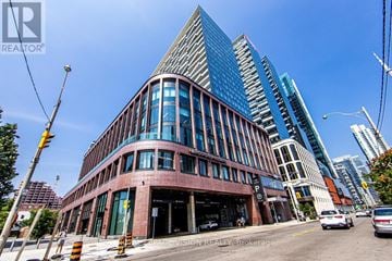 Toronto (Waterfront Communities) condo for rent - A modern building with a curved glass facade is the focal point of the image.