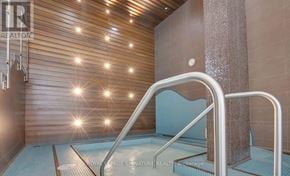 Toronto (Mimico) condo for rent - A modern, well-lit indoor swimming pool area with a wooden wall and a glass block wall.