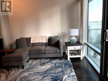 Toronto (Waterfront Communities) condo for rent - A living room with a grey couch and a small table with a lamp on it.